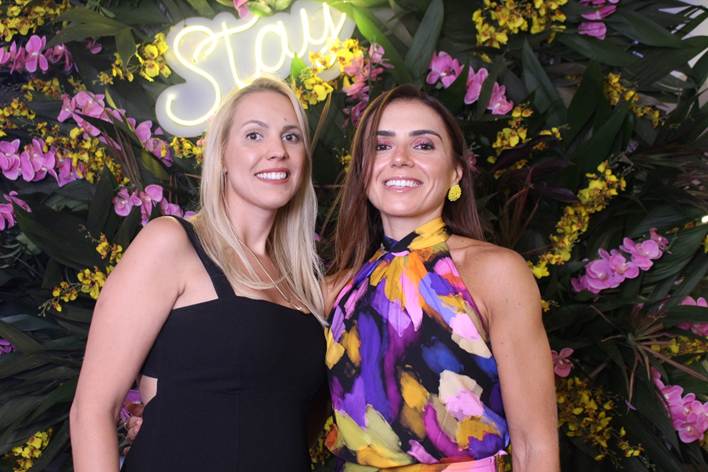 imagem mostra duas mulheres em frente a um painel de flores