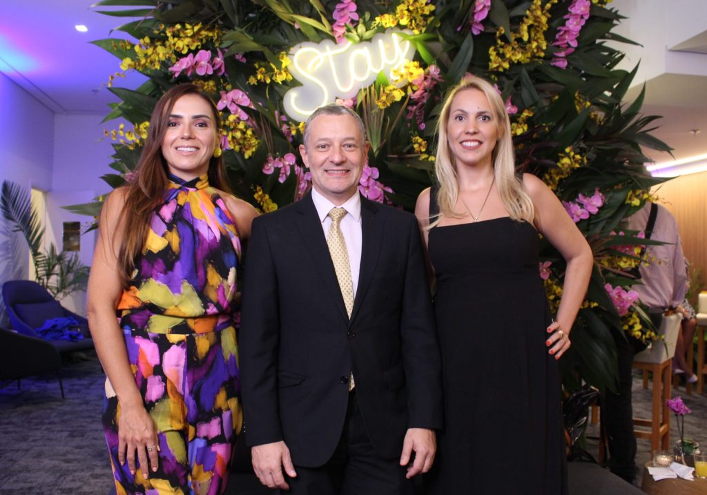 imagem mostra duas mulheres e um homem em uma festa com roupas de gala