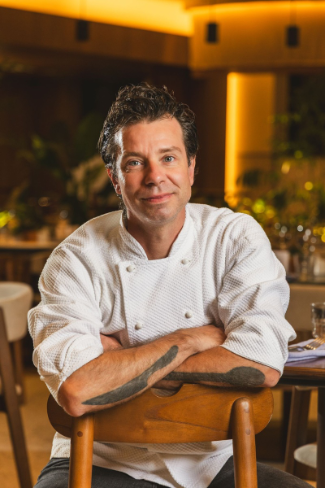 Retrato do chef Pedro Franco, novo chef executivo do Pullman São Paulo Ibirapuera, sentado em uma cadeira em ambiente elegante do restaurante do hotel.