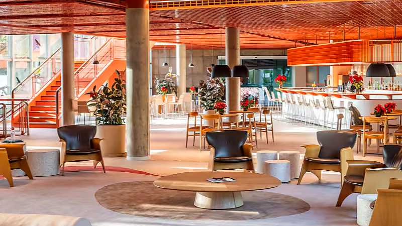Área de lobby do Almenat Tapestry Collection by Hilton com mobiliário contemporâneo, mesas, poltronas e bar integrado, em ambiente amplo e iluminado cercado pela natureza.