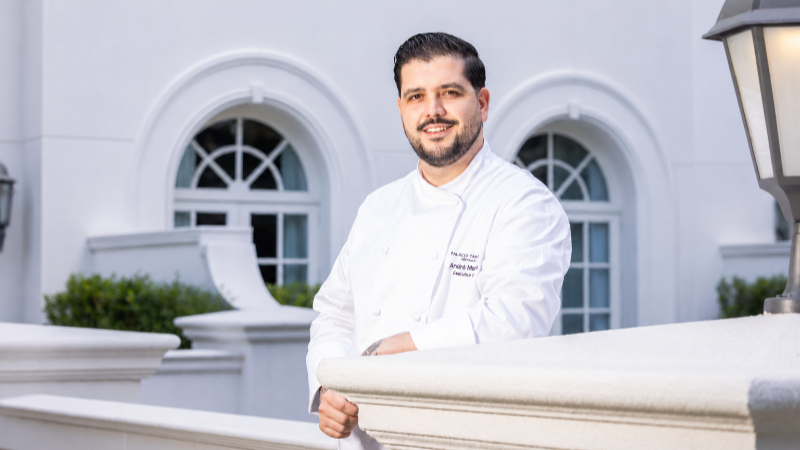 Retrato do chef André Mendes em ambiente interno. O profissional aparece sorrindo, vestindo uniforme de cozinha, em imagem que acompanha o anúncio de sua chegada ao Palácio Tangará para liderar a operação gastronômica do hotel.